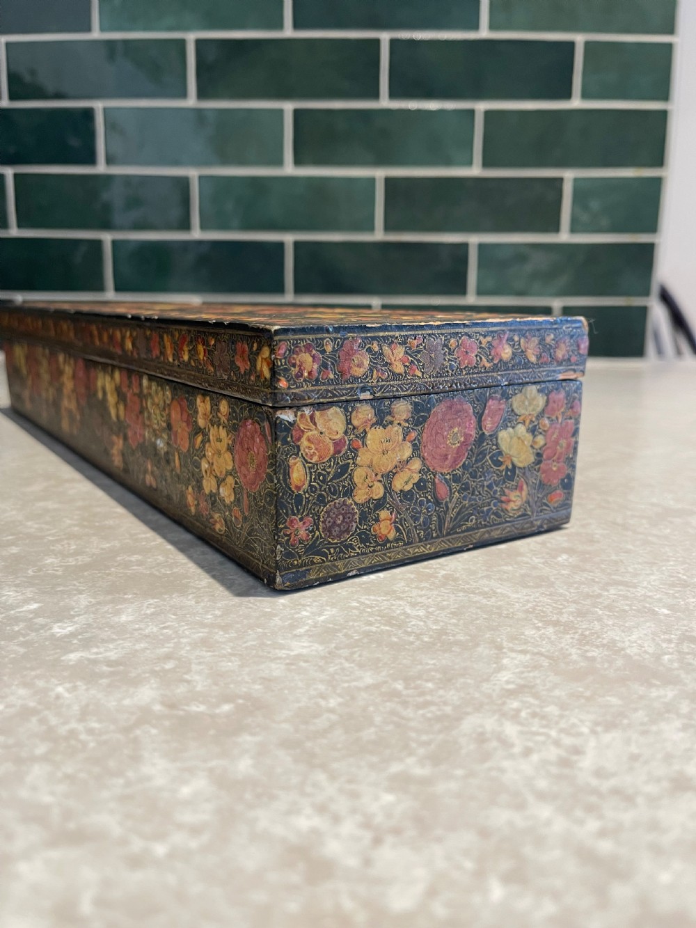 A long rectangular papier-mache box with intricate hand-painted floral patterns in red, yellow, and gold lacquer over a dark background. View II