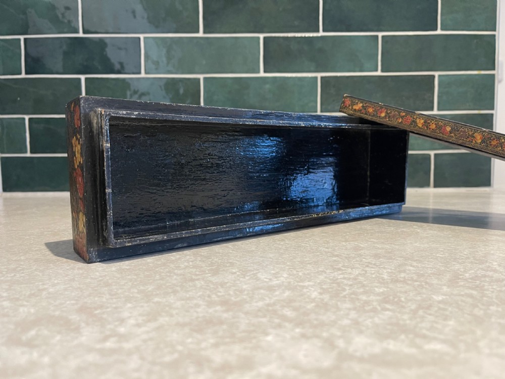 A long rectangular papier-mache box with intricate hand-painted floral patterns in red, yellow, and gold lacquer over a dark background. View III