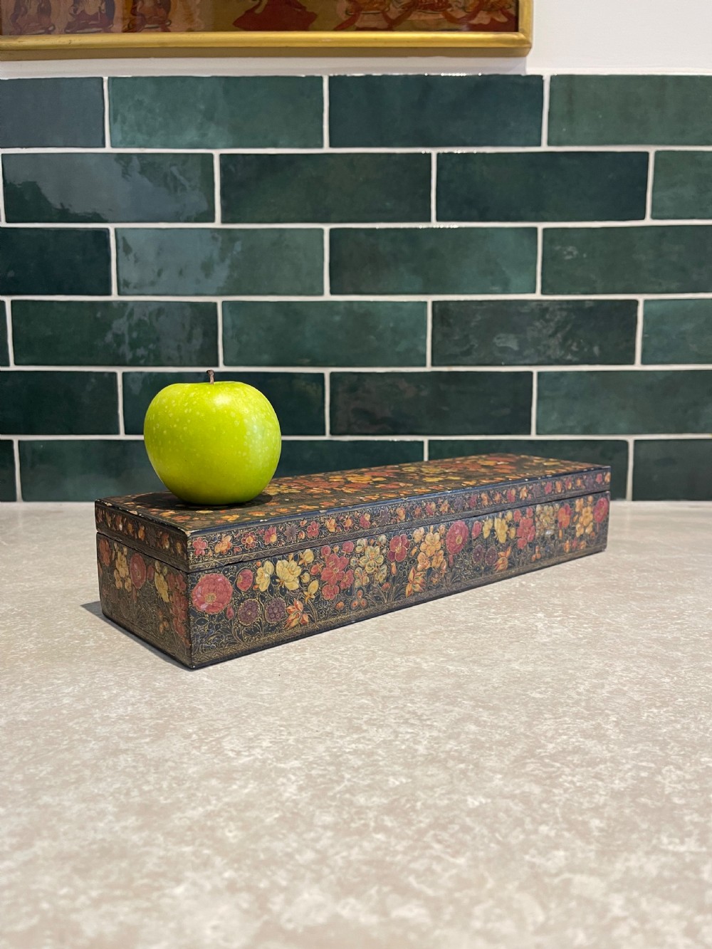 A long rectangular papier-mache box with intricate hand-painted floral patterns in red, yellow, and gold lacquer over a dark background. View IV