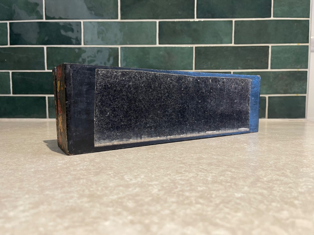 A long rectangular papier-mache box with intricate hand-painted floral patterns in red, yellow, and gold lacquer over a dark background. View V