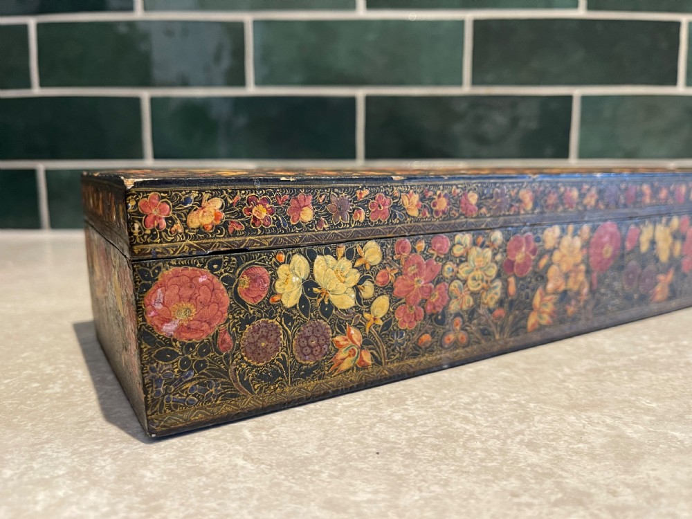 A long rectangular papier-mache box with intricate hand-painted floral patterns in red, yellow, and gold lacquer over a dark background. View VI