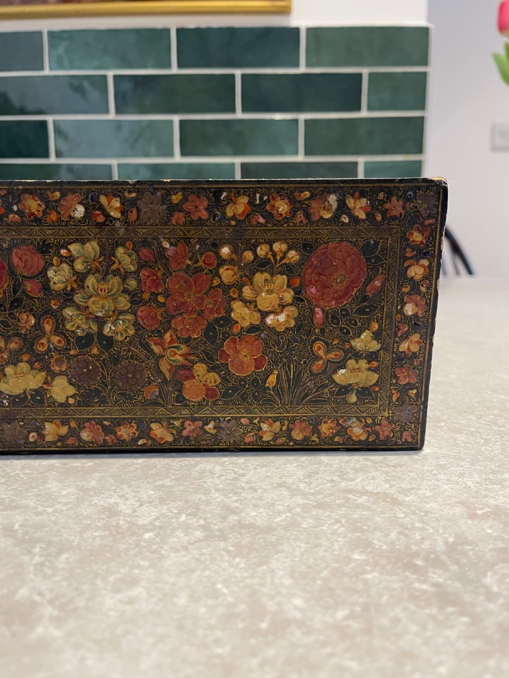 A long rectangular papier-mache box with intricate hand-painted floral patterns in red, yellow, and gold lacquer over a dark background. View VII