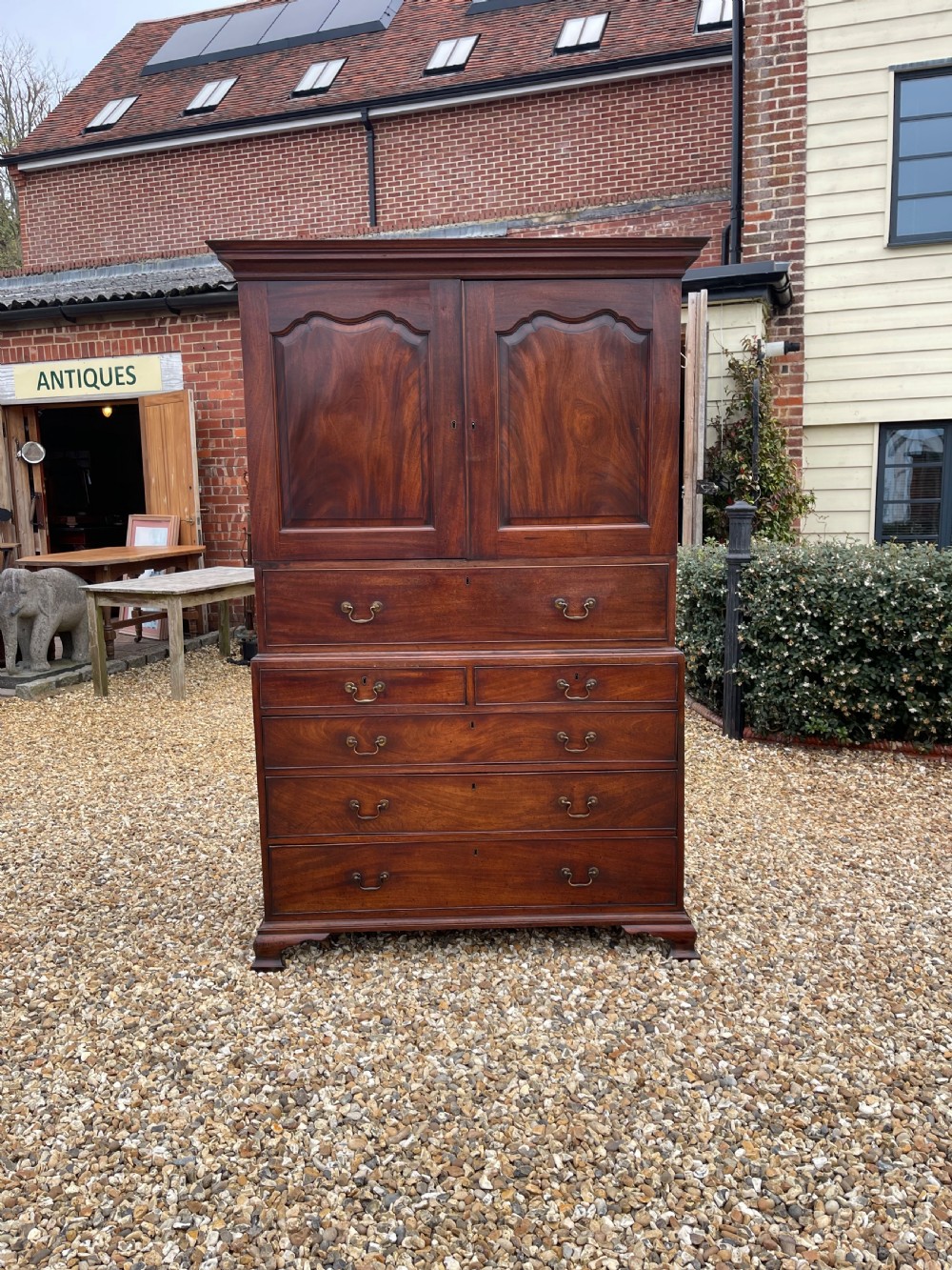 A tall Georgian mahogany secretaire press cupboard featuring two panelled doors above drawers with brass handles, resting on bracket feet.