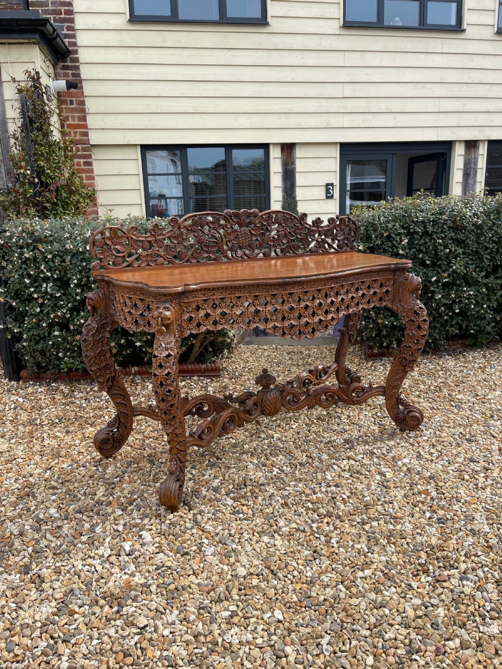 A nineteenth-century Anglo-Indian carved wood console table featuring a detailed openwork apron, gallery back, and intricately carved leg supports.