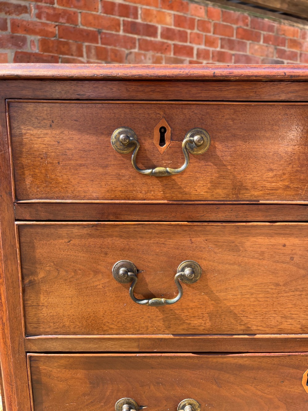 An eighteenth-century Georgian mahogany chest of drawers featuring two short drawers over three long drawers, finished with brass swan-neck handles and bracket feet. View X