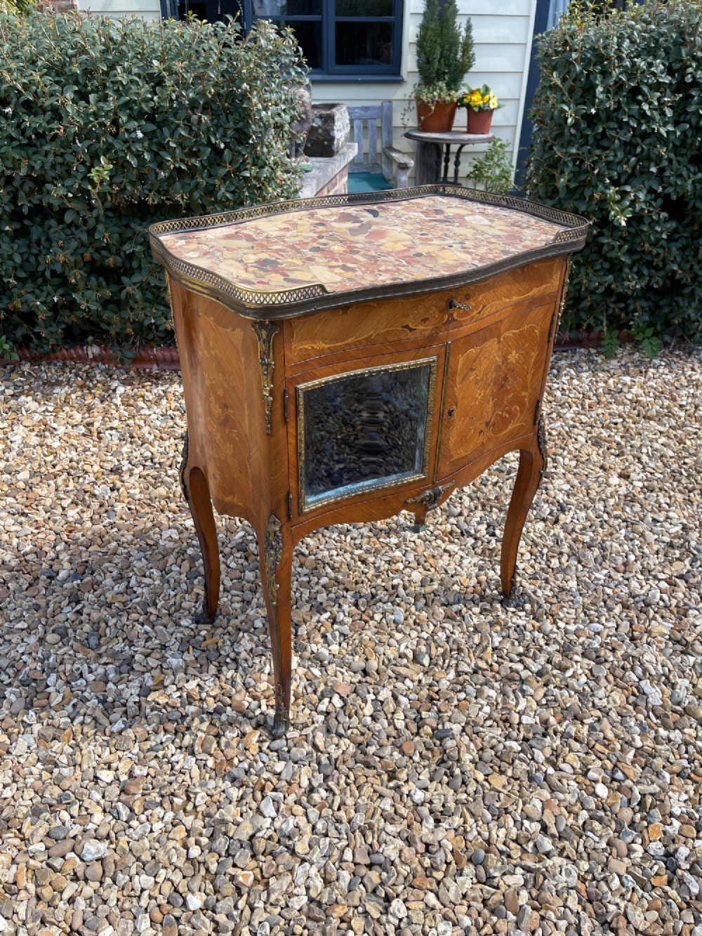 A late nineteenth-century French style side cabinet featuring floral marquetry wood inlay, a variegated marble top surrounded by a pierced brass gallery rim, cabriole legs, and a glazed door.