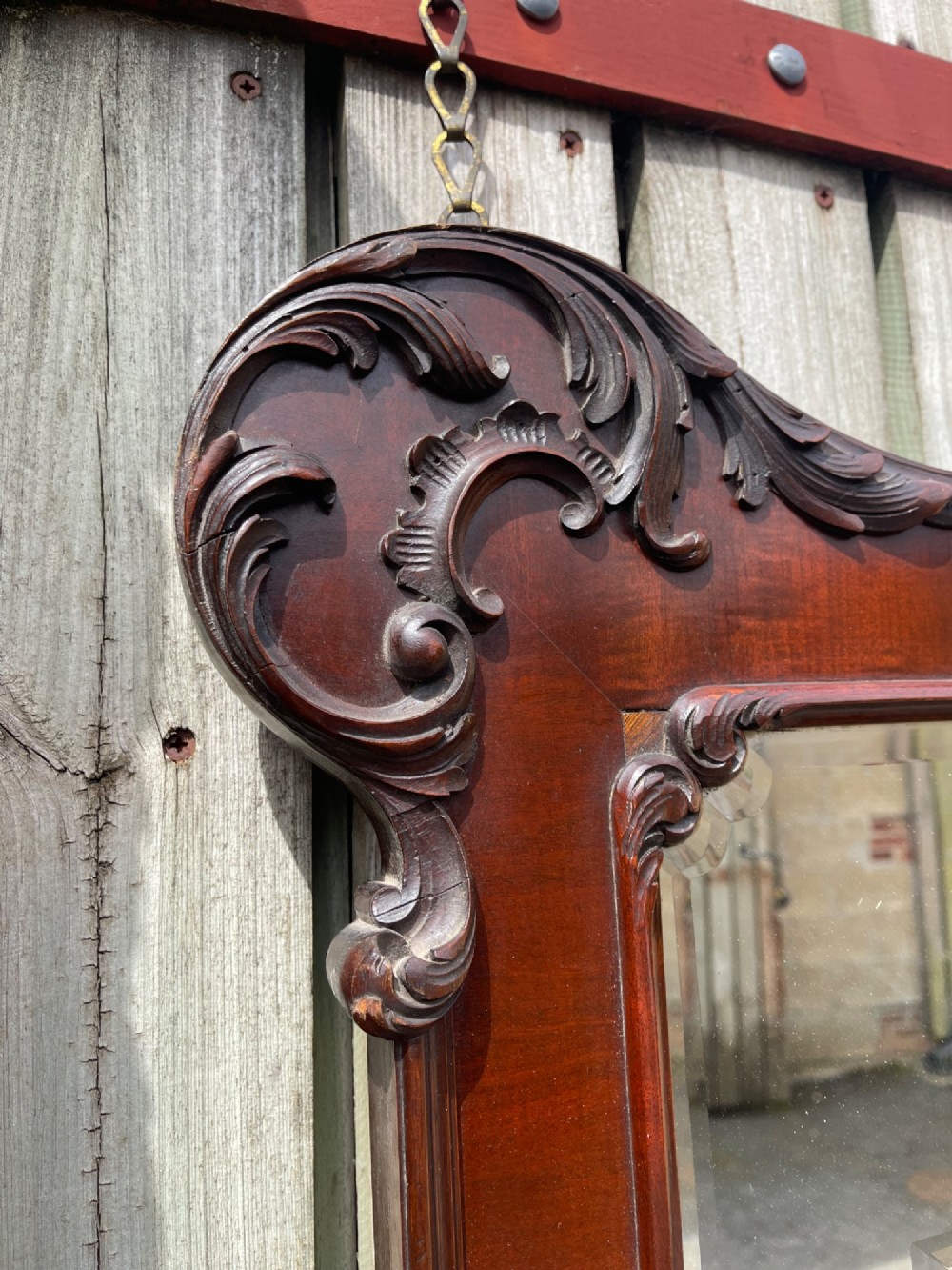 A large horizontal rectangular wall mirror framed in polished dark mahogany with ornate carved scrollwork corners and a central beaded border surrounding multi-panel sectional glass. View II