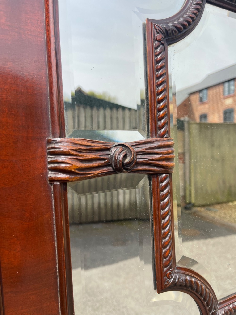 A large horizontal rectangular wall mirror framed in polished dark mahogany with ornate carved scrollwork corners and a central beaded border surrounding multi-panel sectional glass. View III