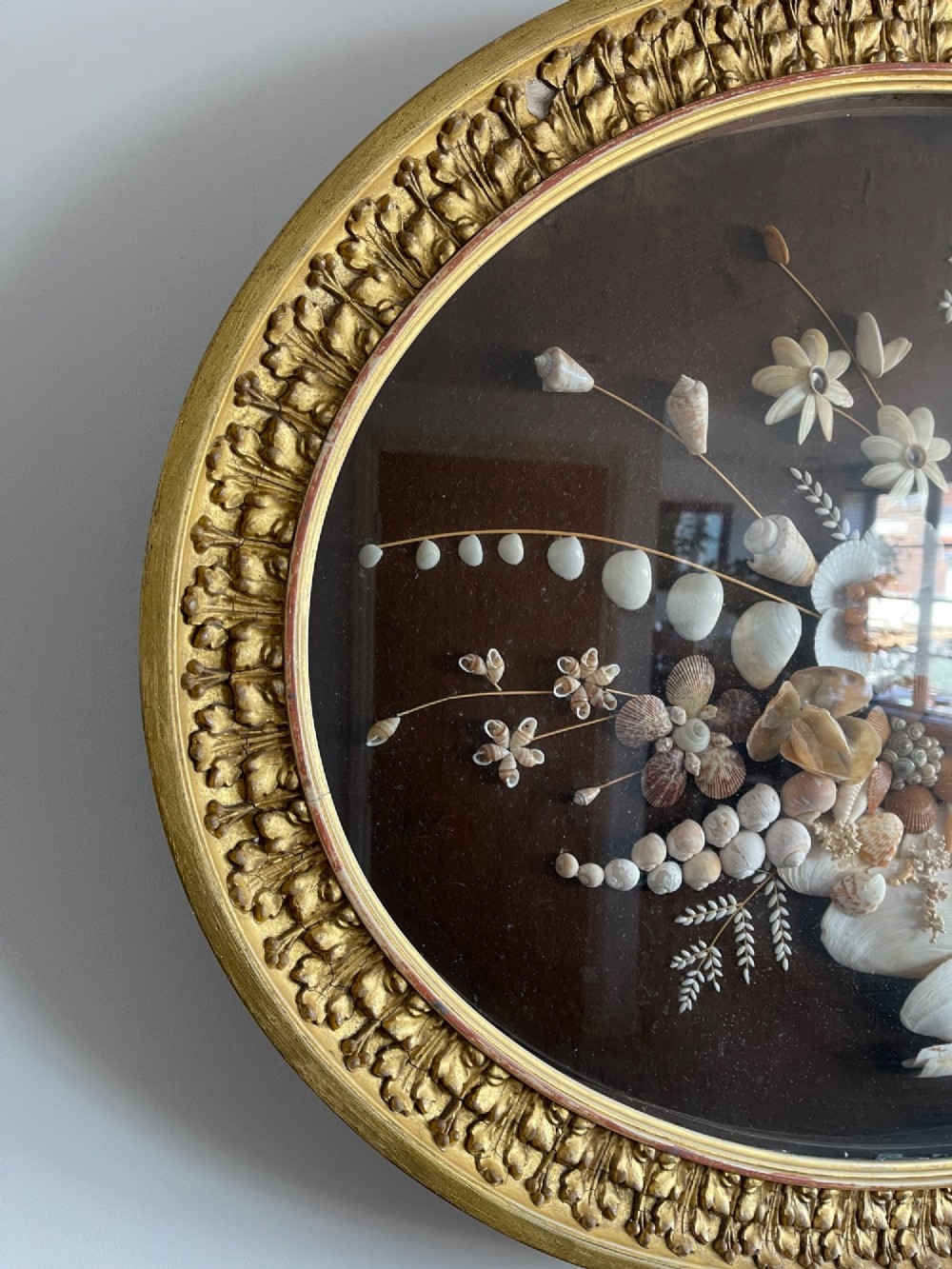 An oval gilt-framed picture featuring a three-dimensional bouquet of sea shells arranged into flowers against a dark brown background. View II