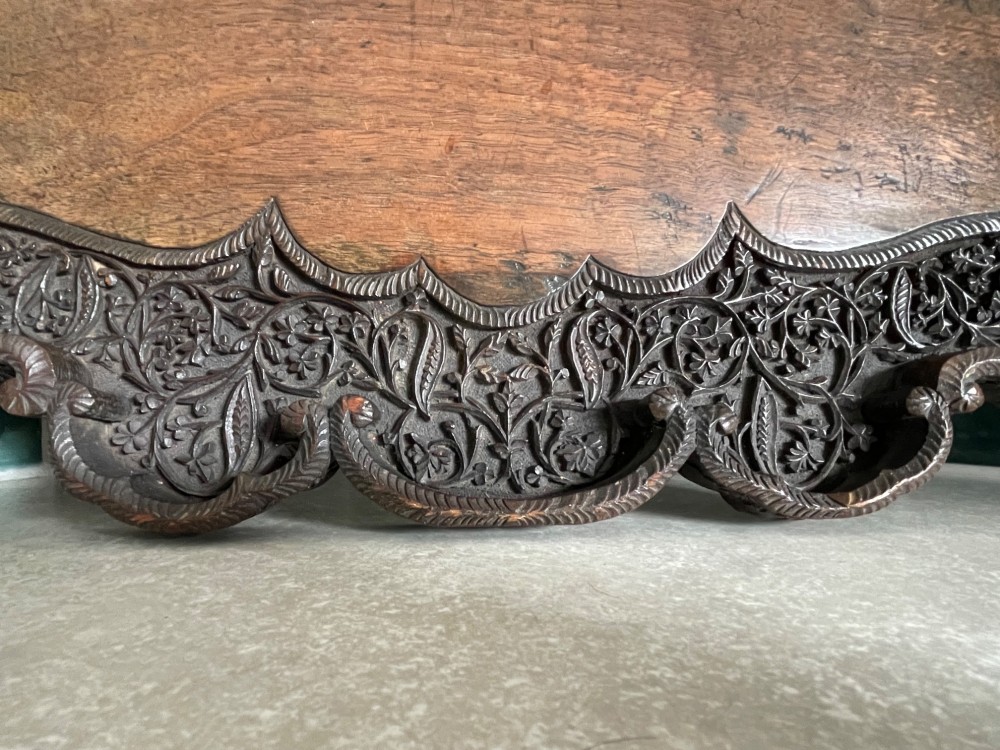 A dark brown carved walnut tray featuring a smooth central panel surrounded by a scalloped, intricately carved floral border. View VI