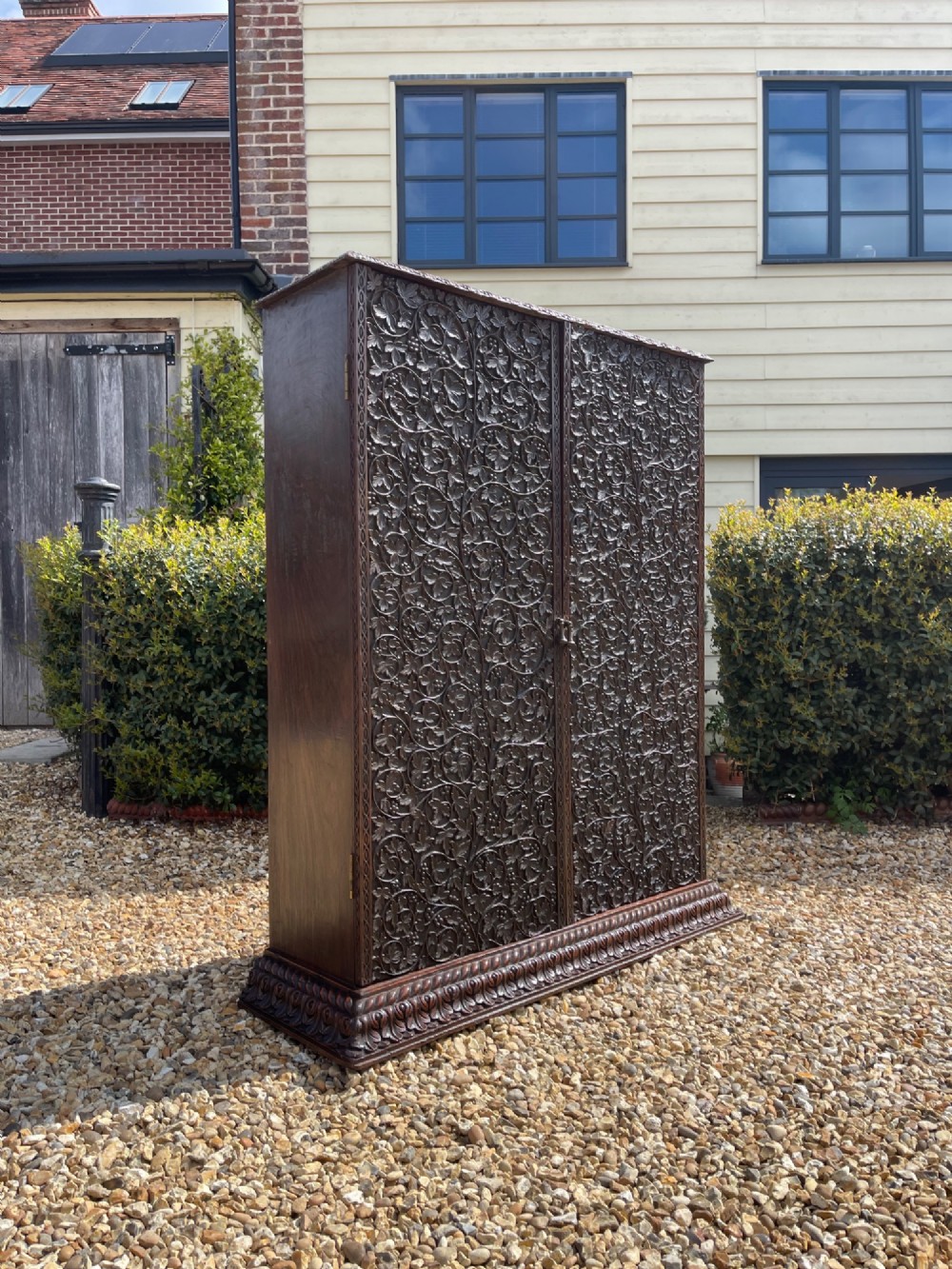 A tall nineteenth-century dark hardwood double-door cupboard decorated with intricate relief foliate carving across the front doors and base.