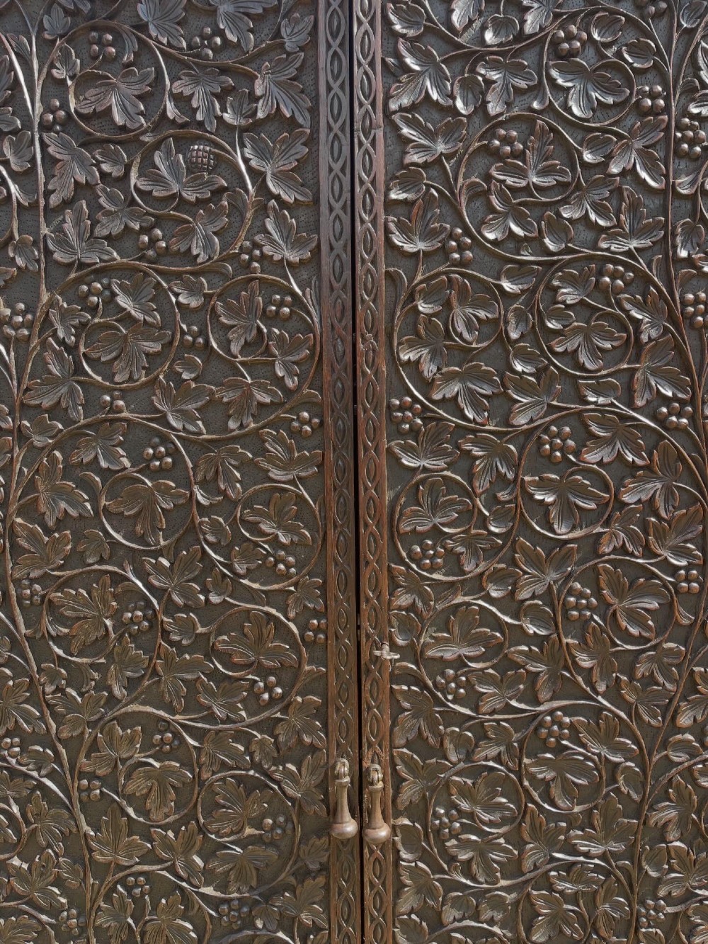 A tall nineteenth-century dark hardwood double-door cupboard decorated with intricate relief foliate carving across the front doors and base. View II
