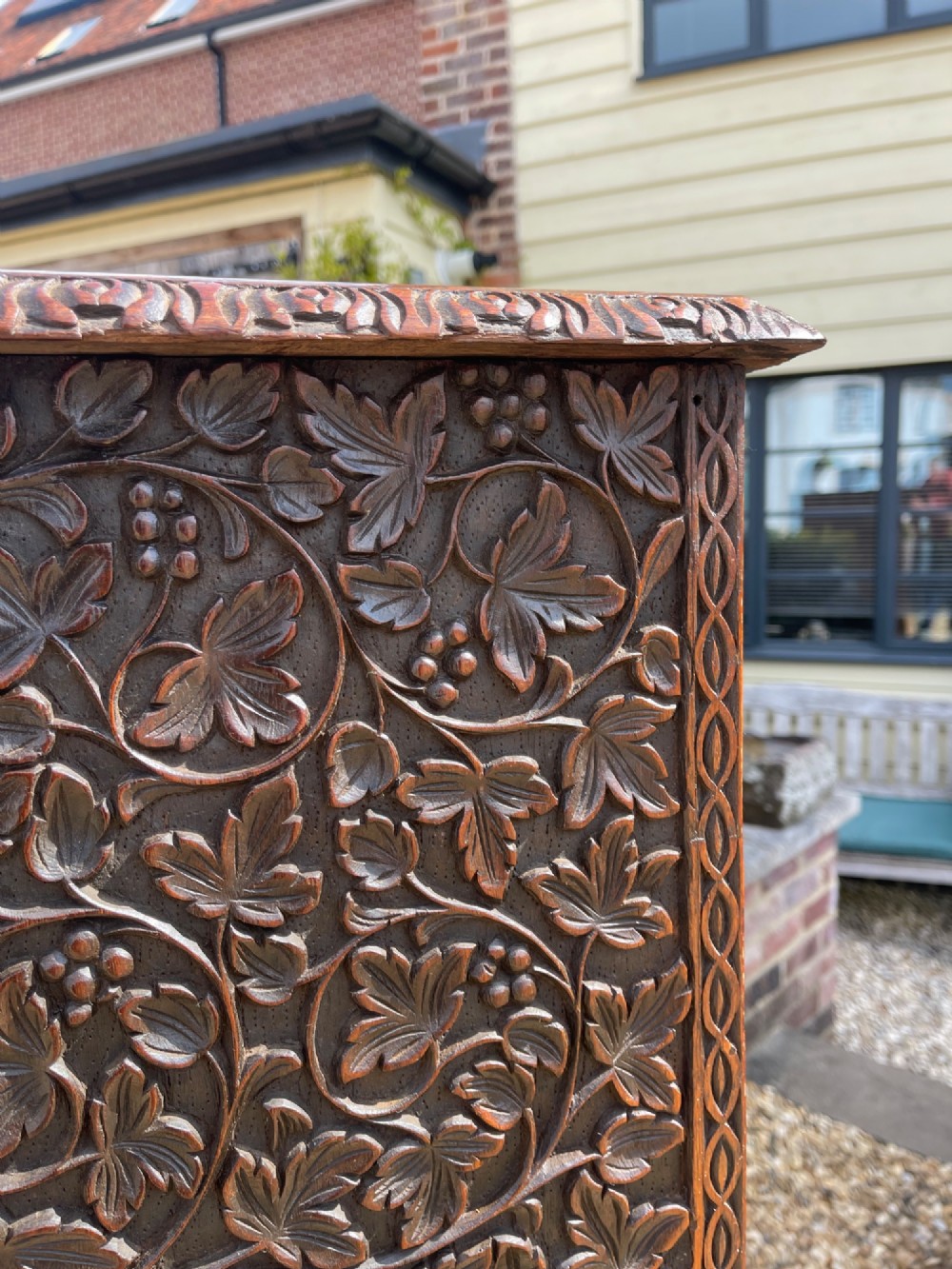 A tall nineteenth-century dark hardwood double-door cupboard decorated with intricate relief foliate carving across the front doors and base. View V