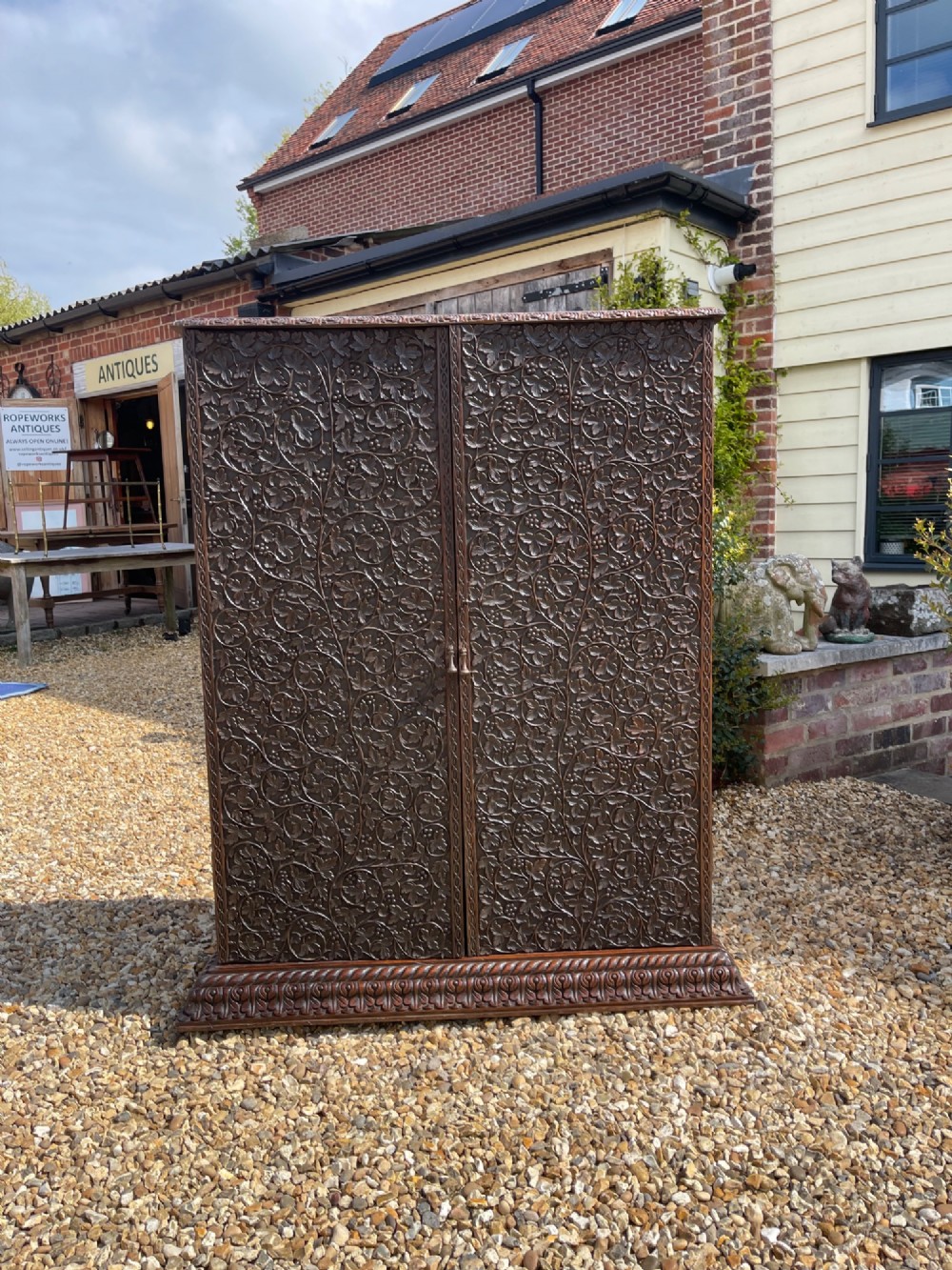 A tall nineteenth-century dark hardwood double-door cupboard decorated with intricate relief foliate carving across the front doors and base. View VIII