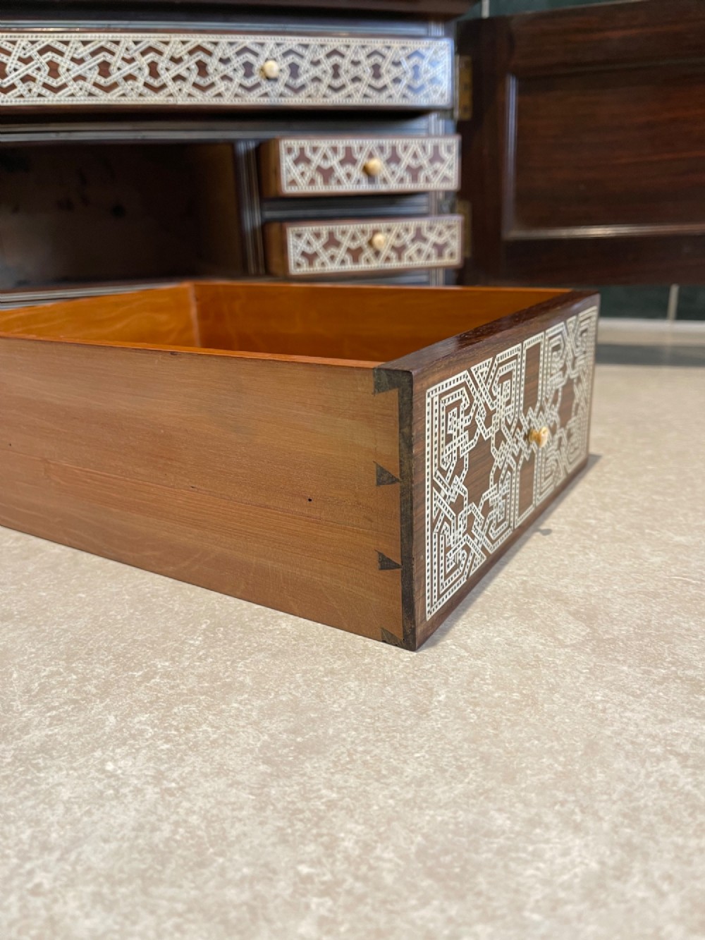 An Ottoman wooden tabletop cabinet featuring geometric mother-of-pearl and bone inlay, with a open side door revealing internal drawers. View IX