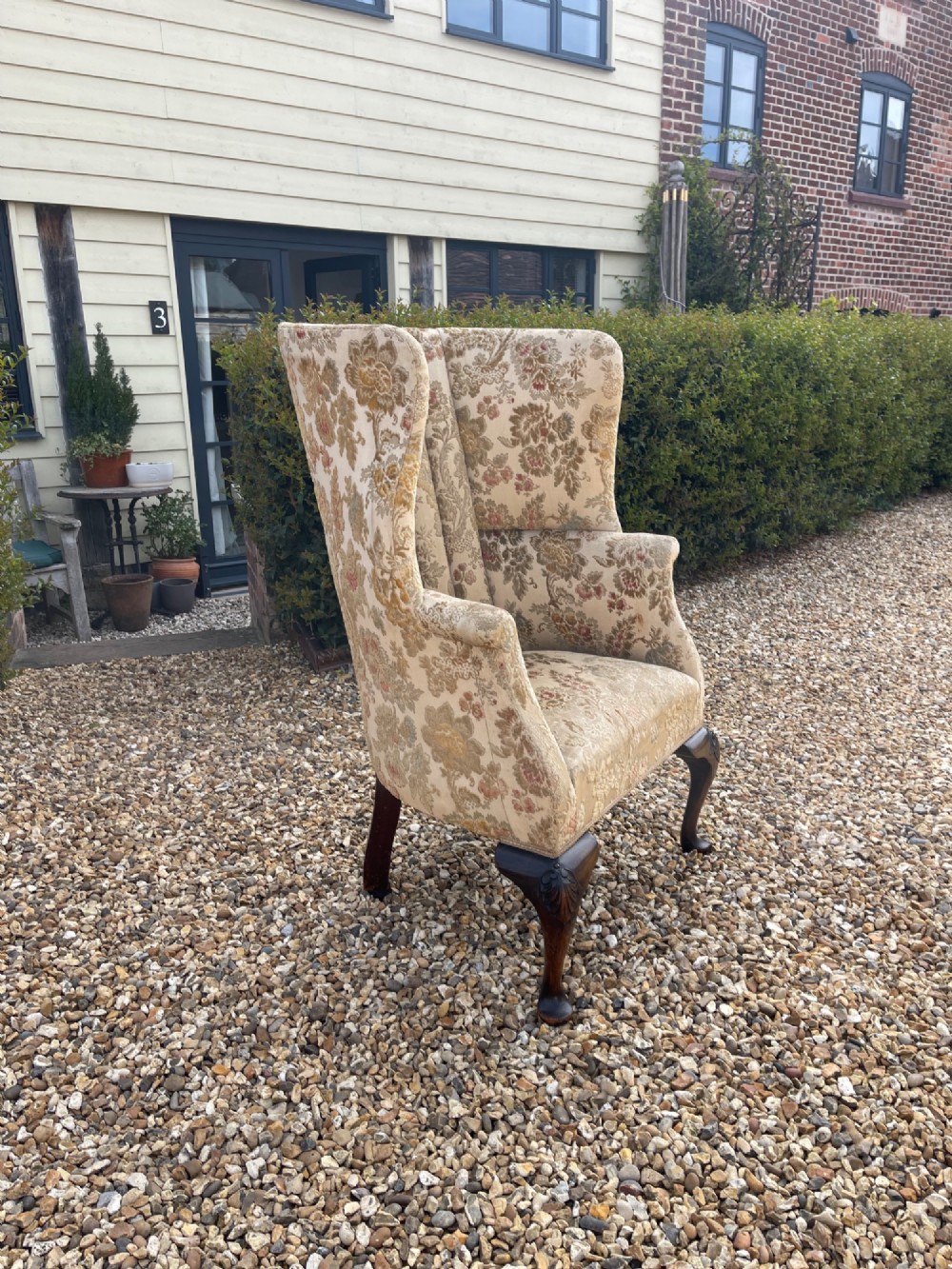A high-backed floral tapestry wingback armchair featuring carved shell details on cabriole front legs.