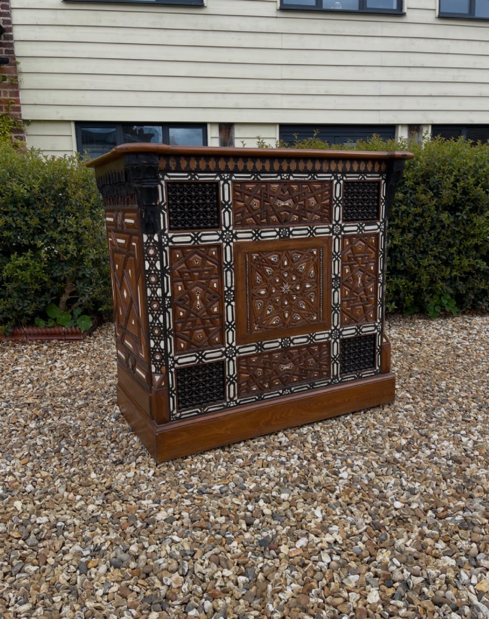 A dark brown rectangular wooden cabinet decorated with geometric bone inlay panels and carved mashrabiya lattice work.