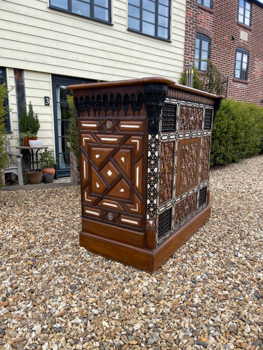 A dark brown rectangular wooden cabinet decorated with geometric bone inlay panels and carved mashrabiya lattice work. View III