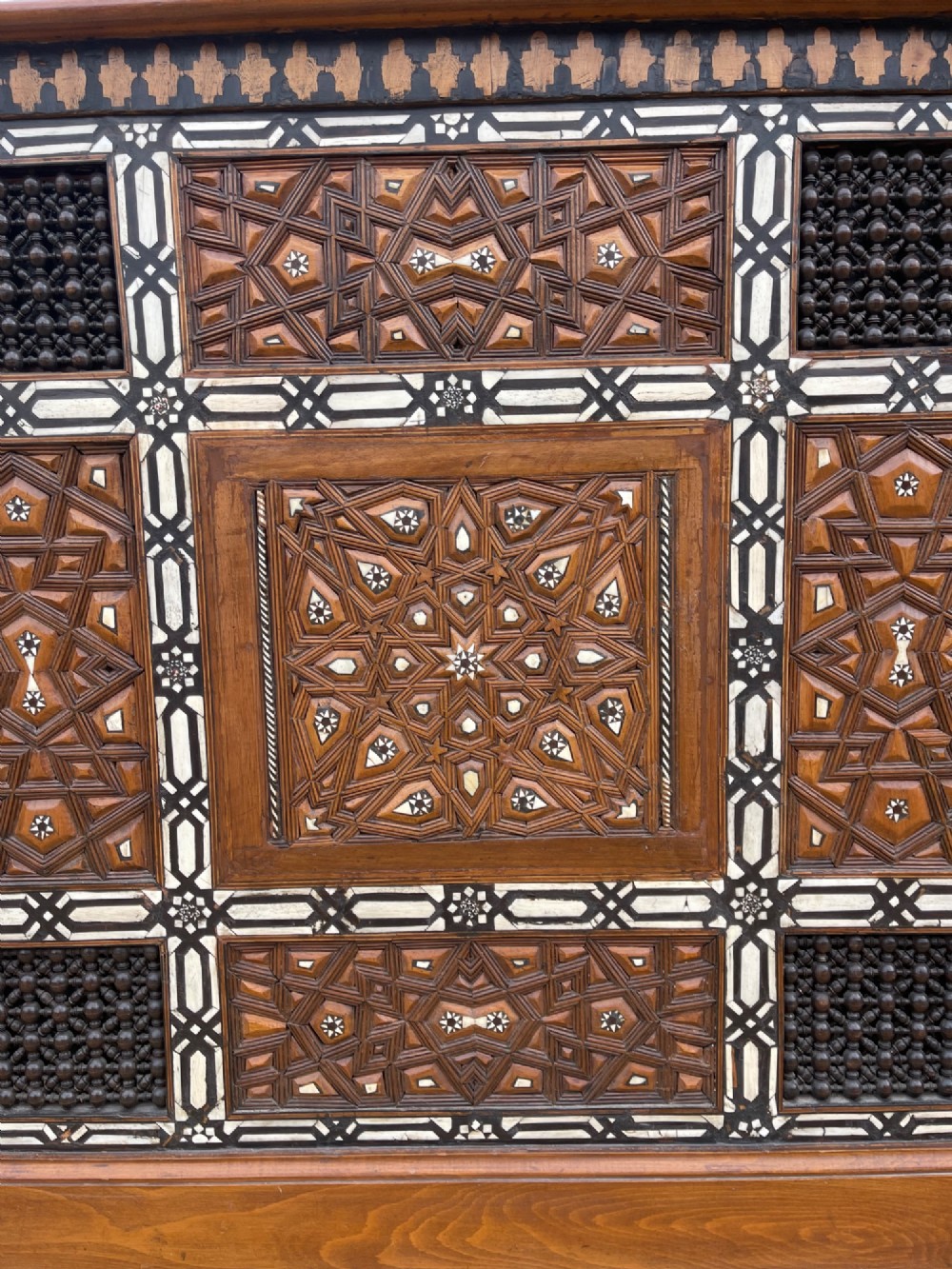 A dark brown rectangular wooden cabinet decorated with geometric bone inlay panels and carved mashrabiya lattice work. View IV