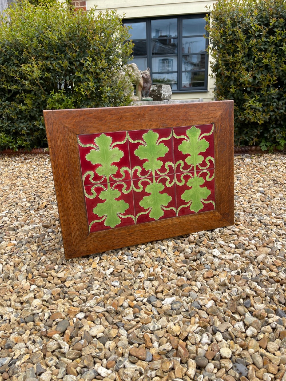 An antique oak side table featuring an inset top panel of six green and terracotta glazed tiles with botanical motifs, raised on curved slatted supports and two lower shelves. View II