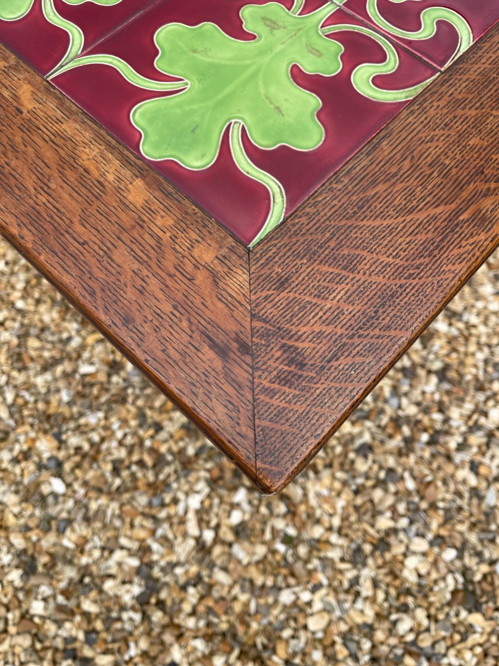 An antique oak side table featuring an inset top panel of six green and terracotta glazed tiles with botanical motifs, raised on curved slatted supports and two lower shelves. View VI