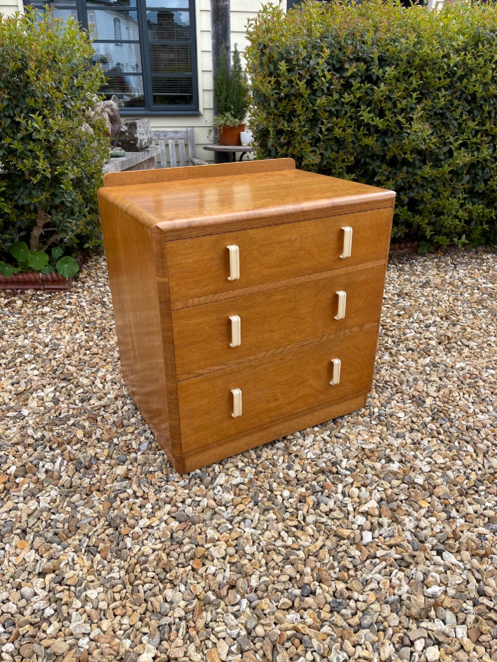 A light golden oak Art Deco chest of drawers featuring three drawers with cream-coloured vertical handles and rounded top edges.