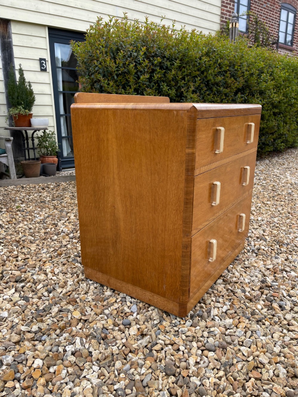 A light golden oak Art Deco chest of drawers featuring three drawers with cream-coloured vertical handles and rounded top edges. View V