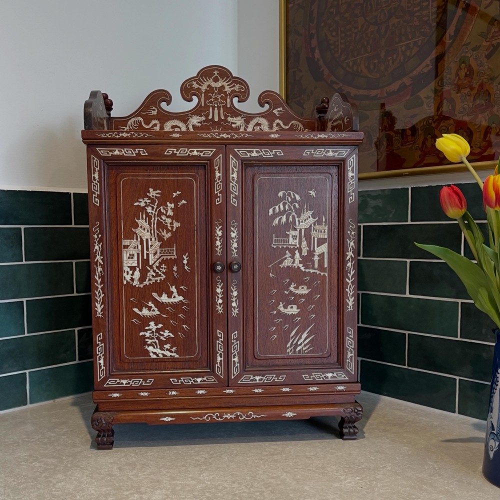 A dark wood Chinese table cabinet featuring two doors embellished with detailed mother-of-pearl landscape inlays, flanked by decorative borders and topped with a carved cresting.