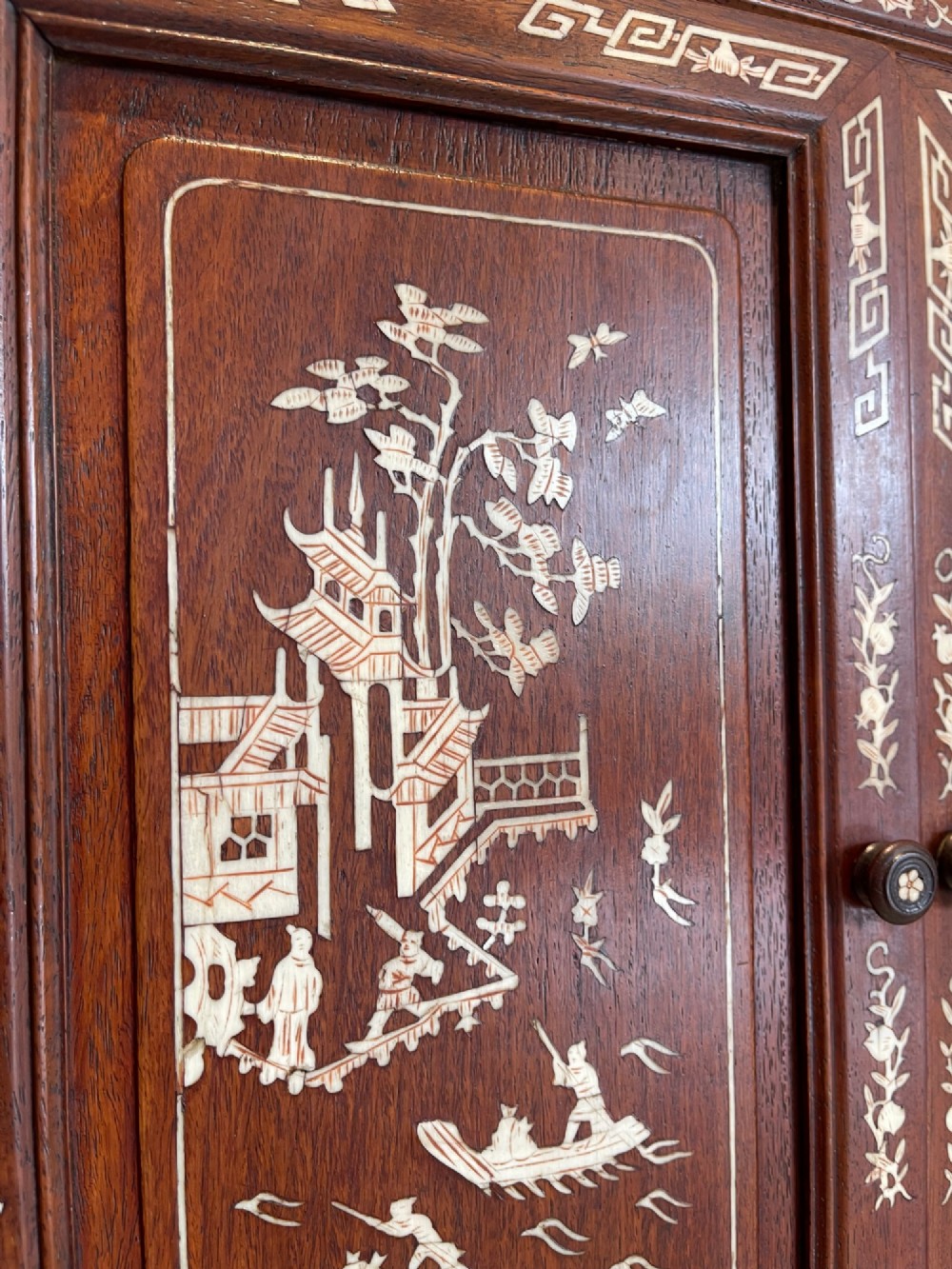 A dark wood Chinese table cabinet featuring two doors embellished with detailed mother-of-pearl landscape inlays, flanked by decorative borders and topped with a carved cresting. View V