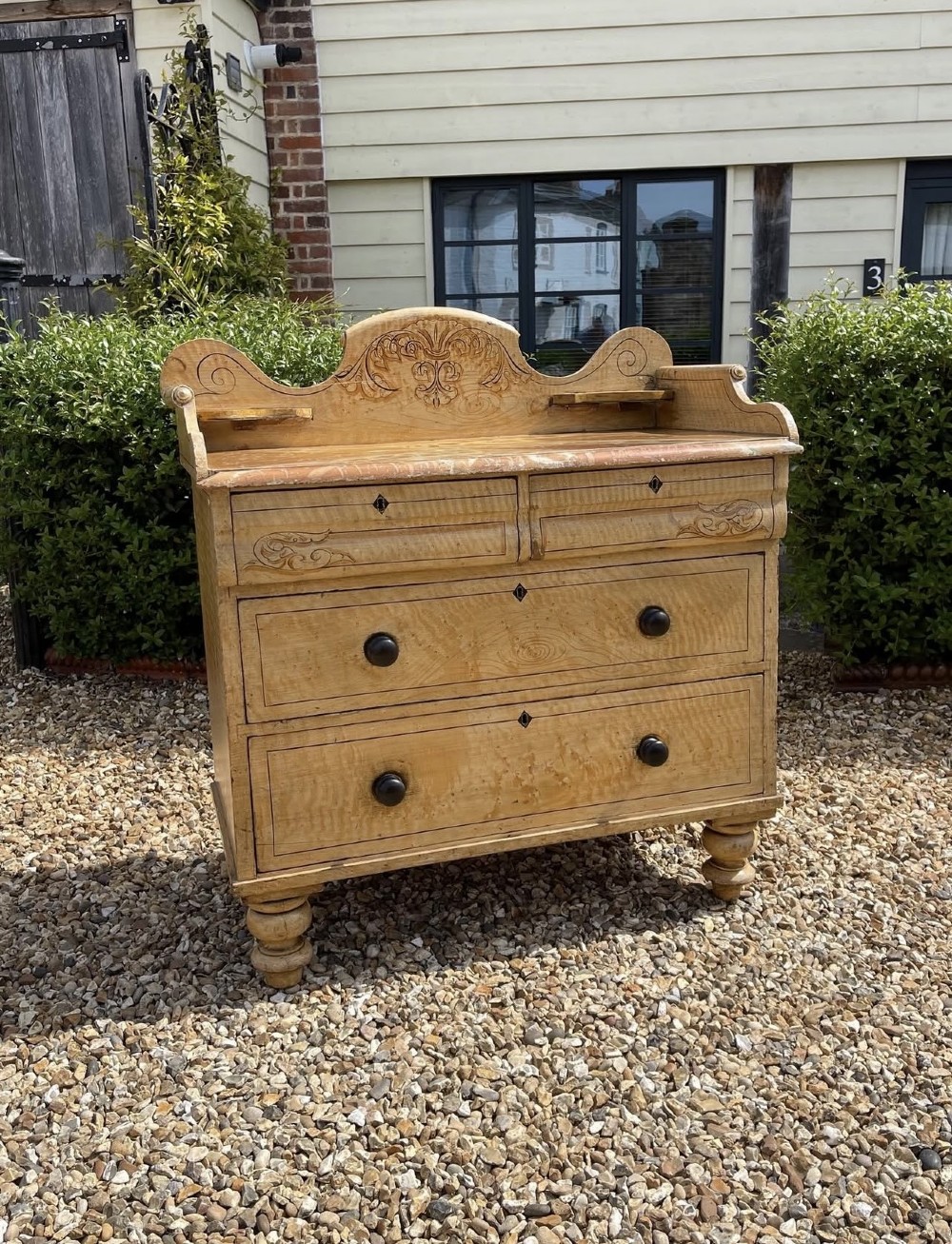A Victorian painted pine chest of drawers with a carved gallery back, wooden knobs, and turned feet.