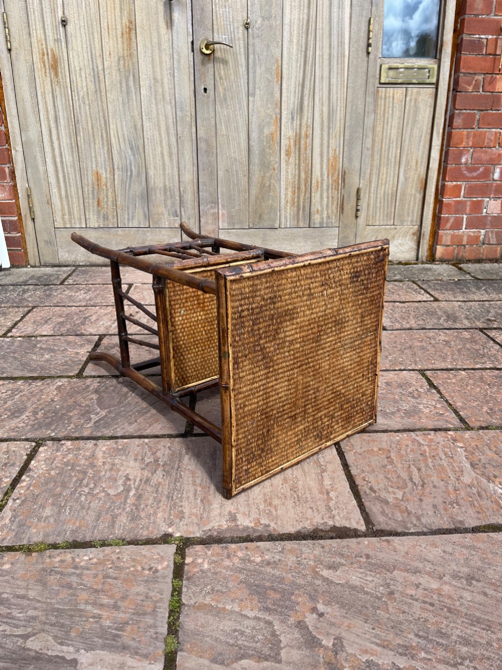 A late Victorian two-tier side table constructed from a dark bamboo frame with woven cane surfaces on the square top and lower shelf. View IV