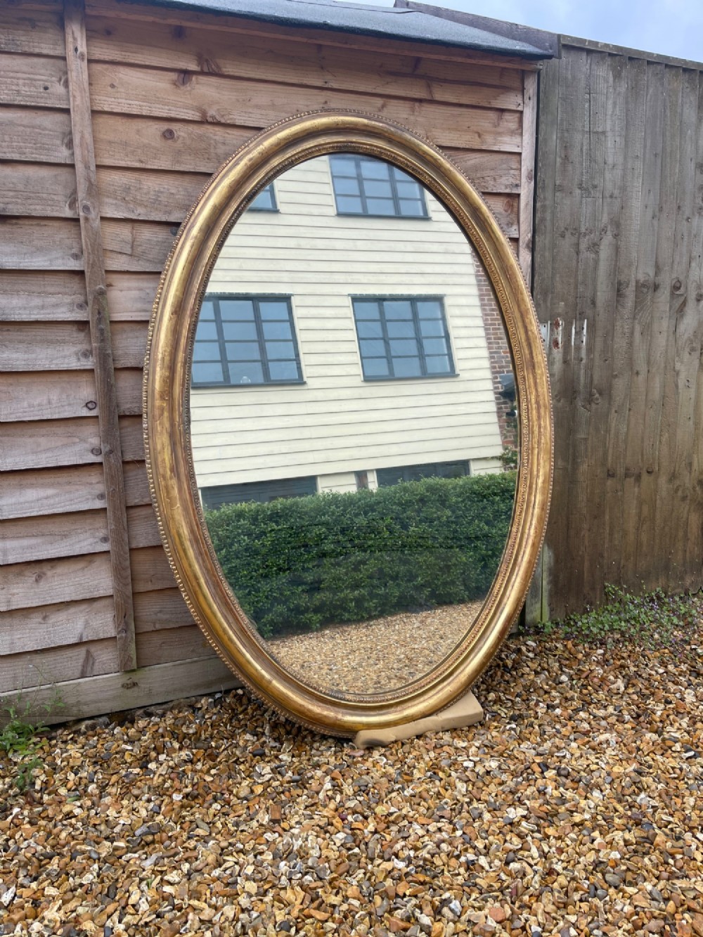 A large oval wall mirror featuring a gilded wood and gesso frame with beaded and moulded decorative borders.