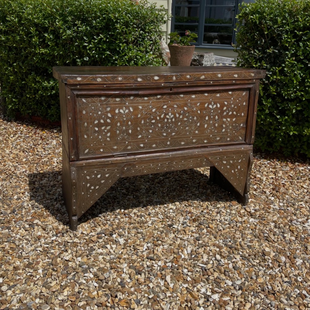 A dark walnut Syrian storage trunk decorated with detailed white mother-of-pearl floral and geometric inlay across the front panel and raised trestle base.