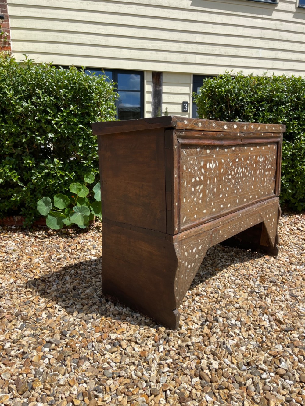 A dark walnut Syrian storage trunk decorated with detailed white mother-of-pearl floral and geometric inlay across the front panel and raised trestle base. View V