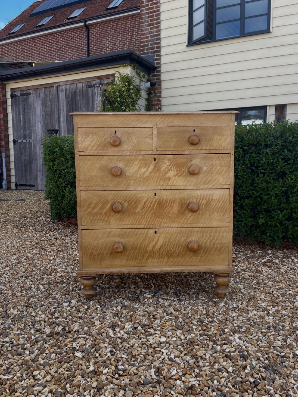 A Victorian pine chest of drawers with an original light brown faux-grain painted finish, featuring two short drawers over three long drawers with turned wooden handles and bun feet.