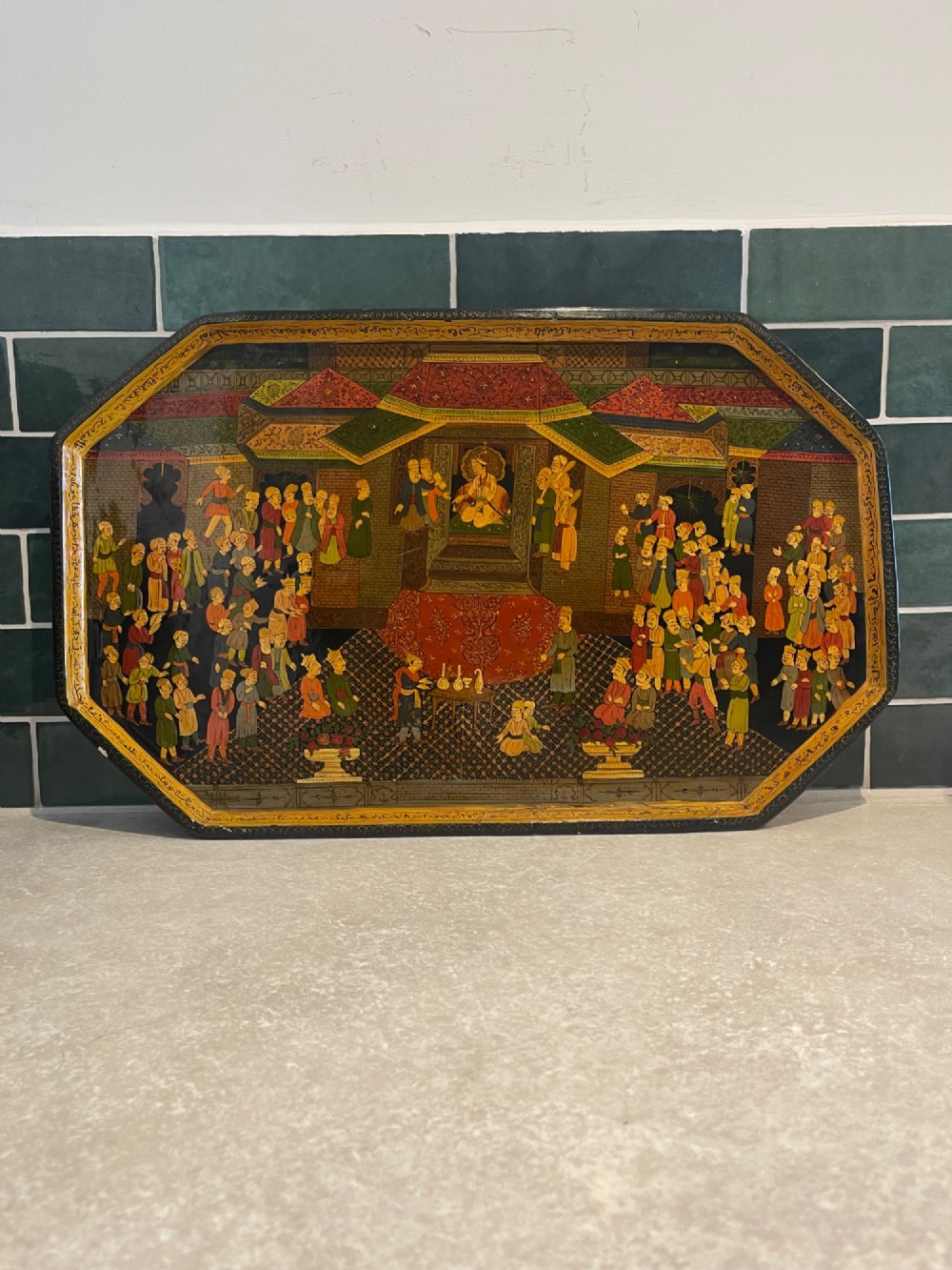 An octagonal Kashmiri papier-mache tray featuring a detailed hand-painted court scene with figures surrounded by a calligraphic border.
