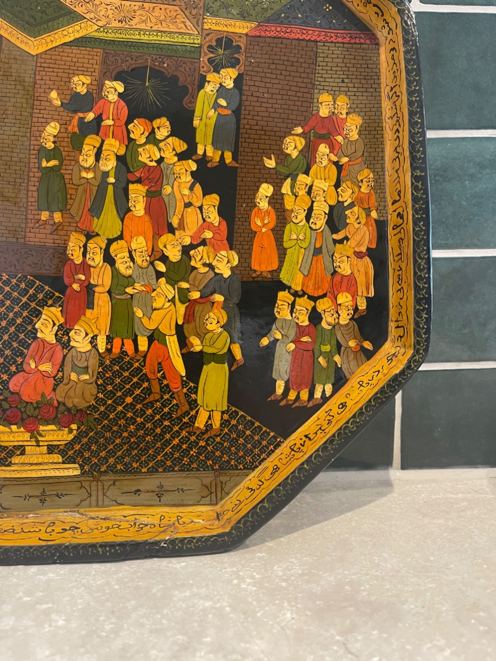An octagonal Kashmiri papier-mache tray featuring a detailed hand-painted court scene with figures surrounded by a calligraphic border. View VI