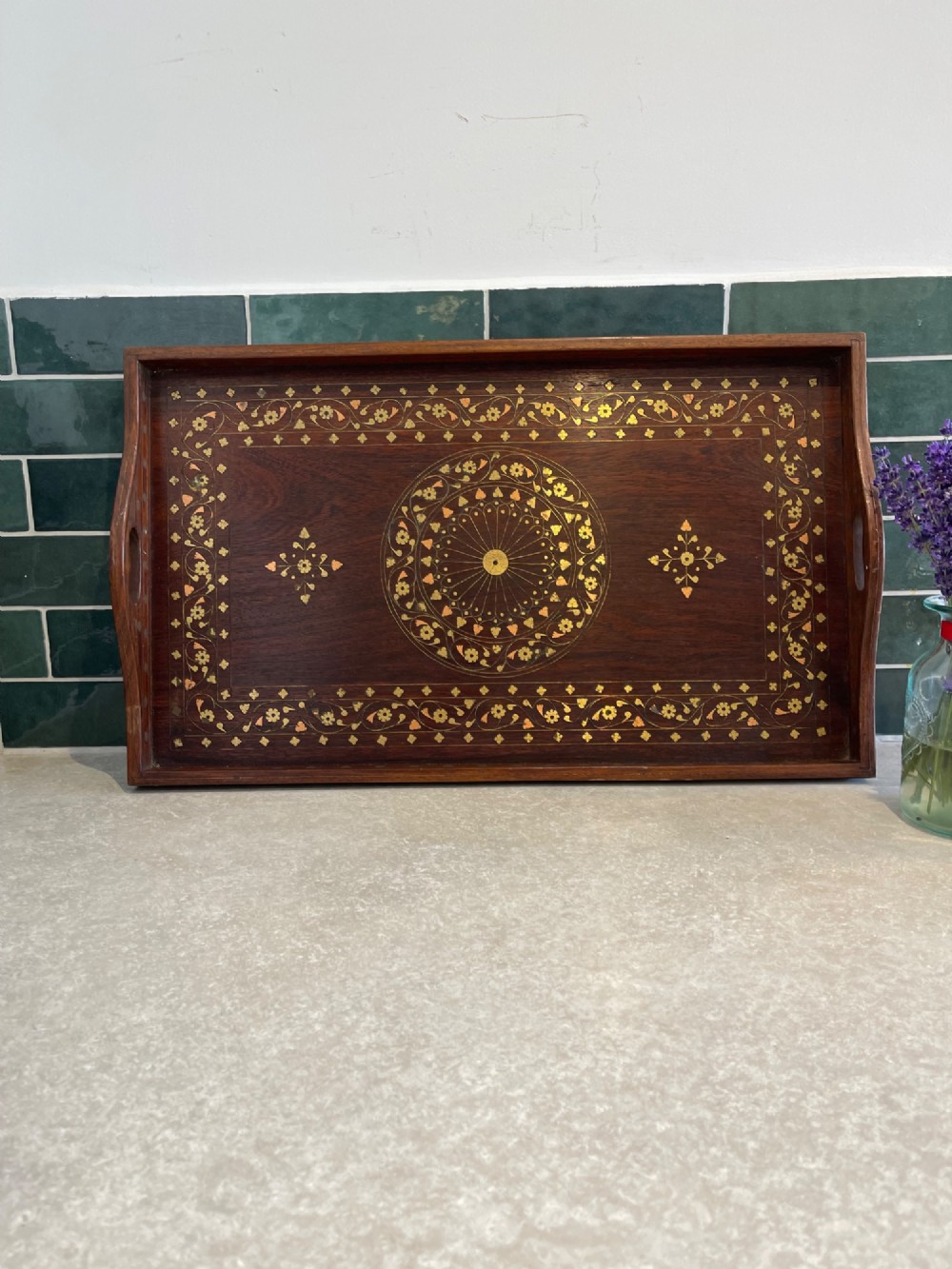 A rectangular dark hardwood serving tray featuring intricate floral and geometric brass inlay with cut-out side handles.