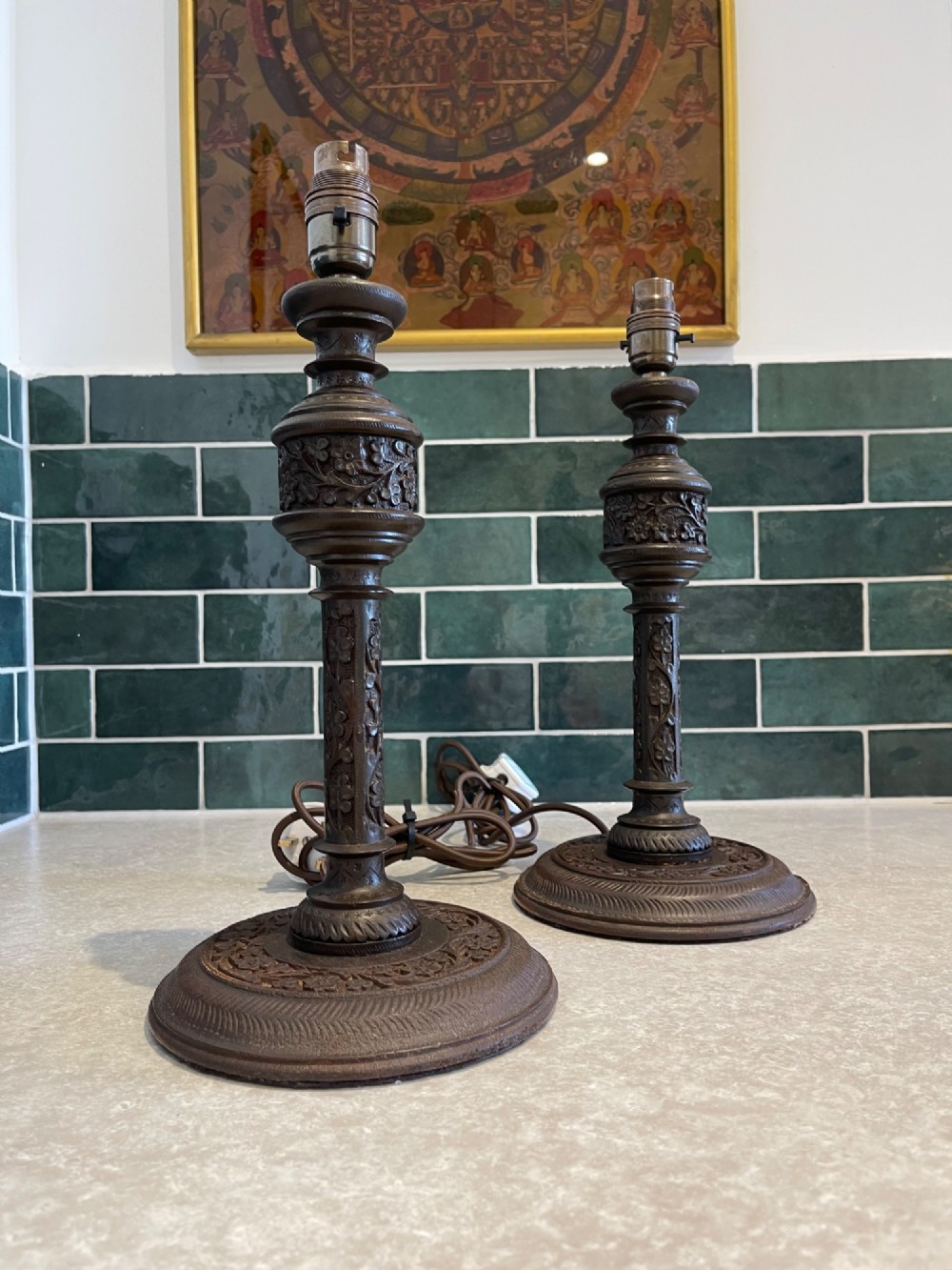 A pair of hand-carved dark brown wooden table lamp bases featuring intricate floral relief detailing and turned shafts.