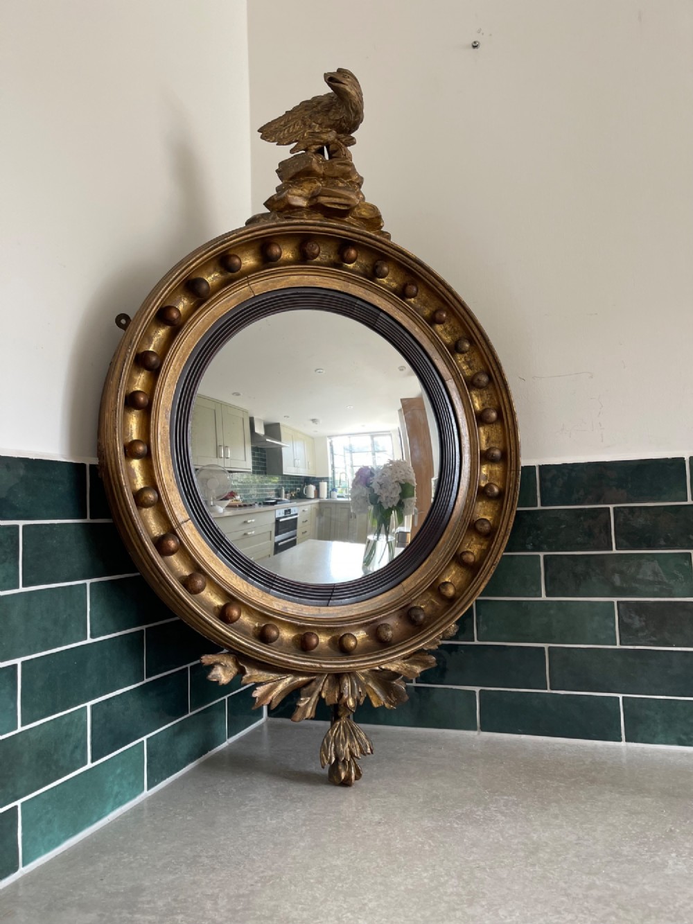 A circular Georgian giltwood convex wall mirror topped with a carved eagle cresting and featuring a frame decorated with ball spherules and an acanthus leaf apron.