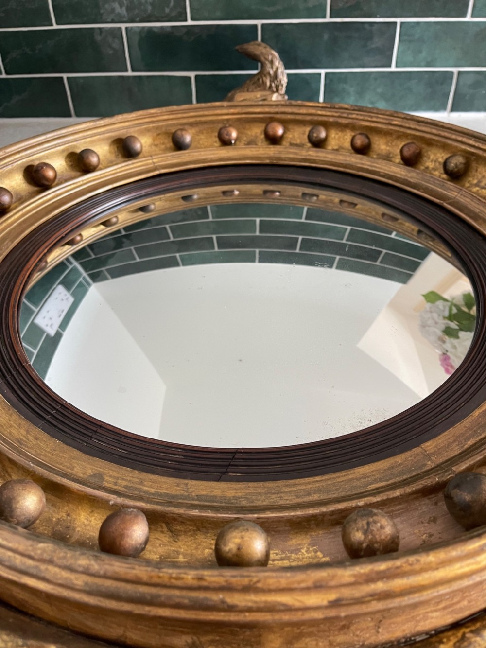 A circular Georgian giltwood convex wall mirror topped with a carved eagle cresting and featuring a frame decorated with ball spherules and an acanthus leaf apron. View II