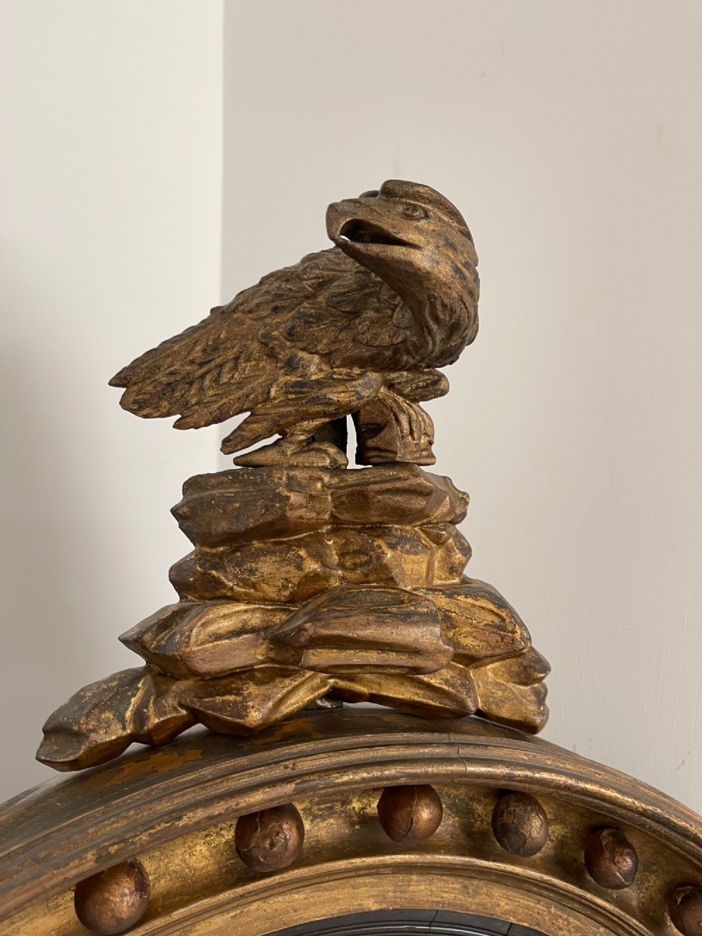 A circular Georgian giltwood convex wall mirror topped with a carved eagle cresting and featuring a frame decorated with ball spherules and an acanthus leaf apron. View V
