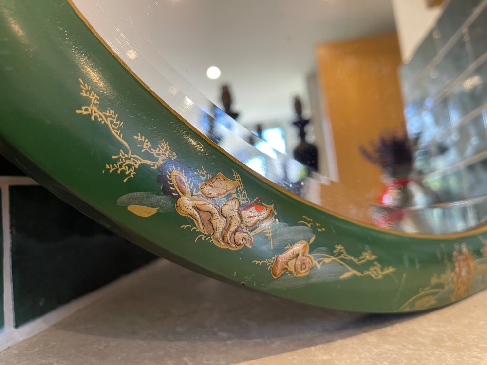 An oval wall mirror featuring a deep green lacquered wooden frame adorned with hand-painted gold chinoiserie figural landscapes. View II