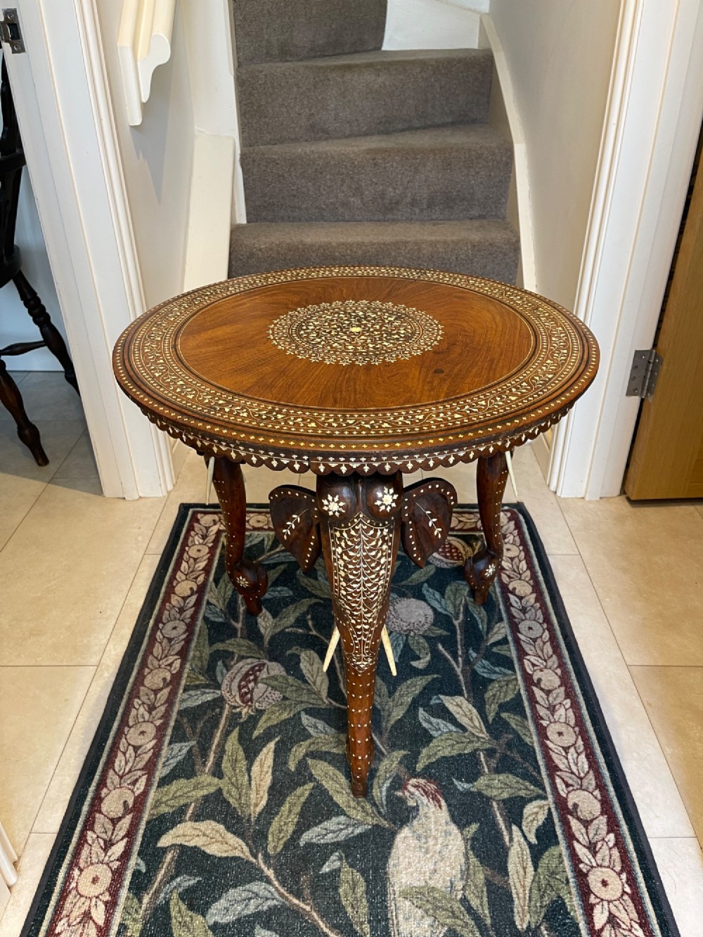 A circular dark wood side table featuring elaborate floral bone inlay work and three carved elephant head legs.