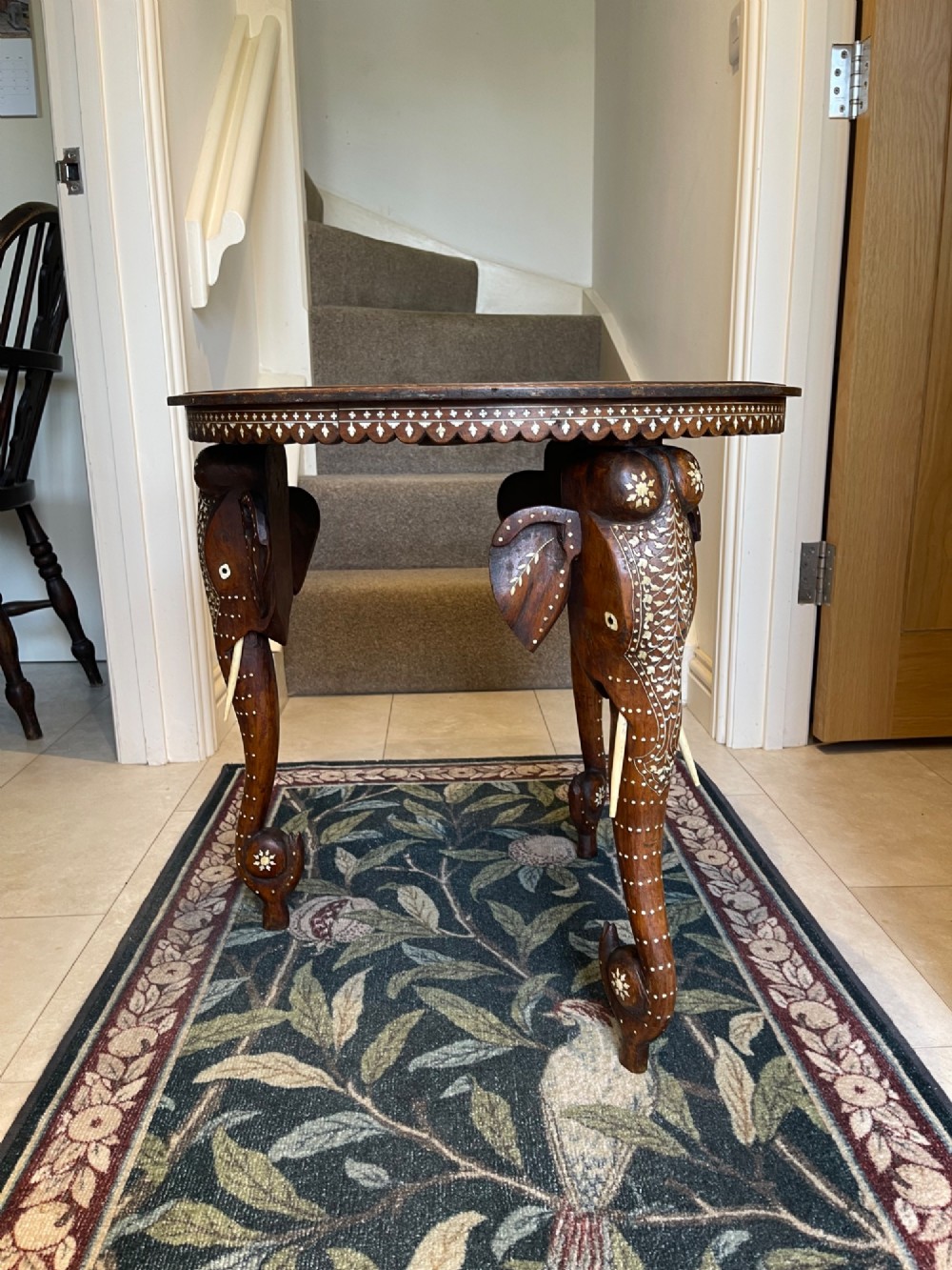 A circular dark wood side table featuring elaborate floral bone inlay work and three carved elephant head legs. View III