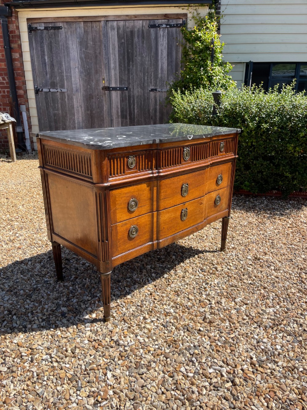 An 18th-century French cherrywood commode featuring a dark grey marble top, three frieze drawers above two long drawers, fluted sides, brass ring handles, and tapered legs.
