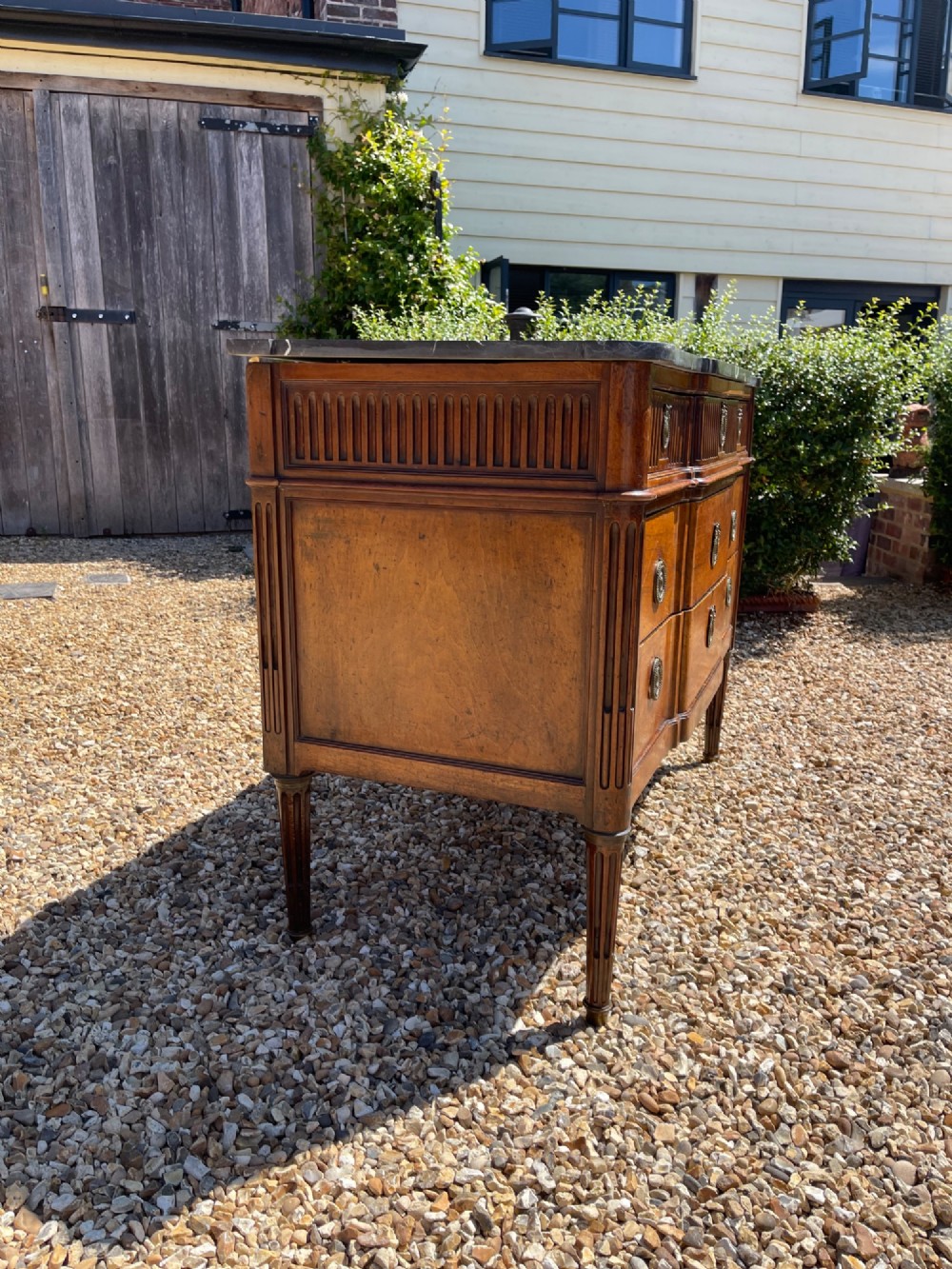 An 18th-century French cherrywood commode featuring a dark grey marble top, three frieze drawers above two long drawers, fluted sides, brass ring handles, and tapered legs. View II