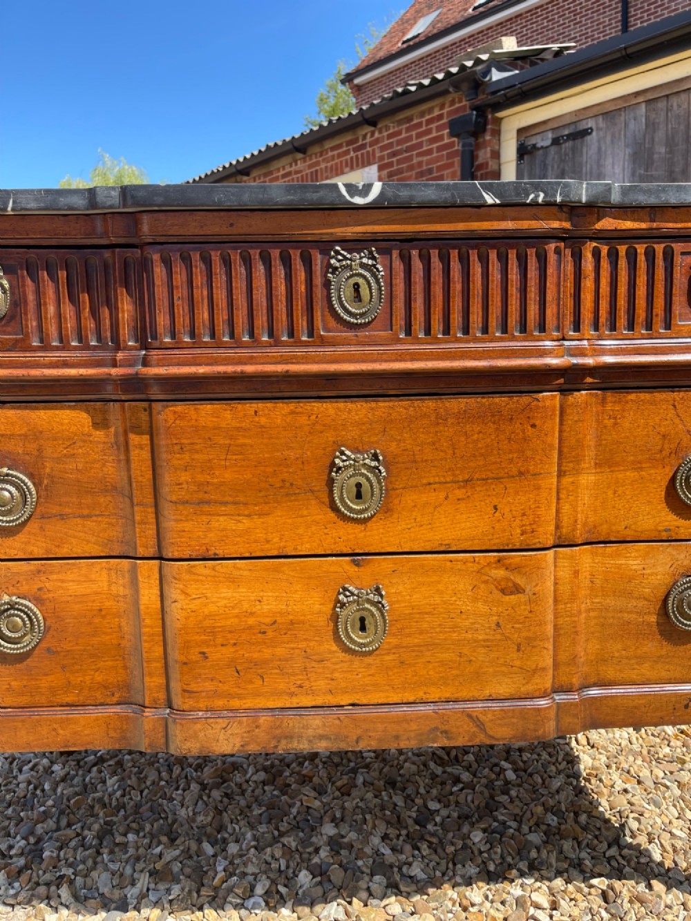 An 18th-century French cherrywood commode featuring a dark grey marble top, three frieze drawers above two long drawers, fluted sides, brass ring handles, and tapered legs. View V