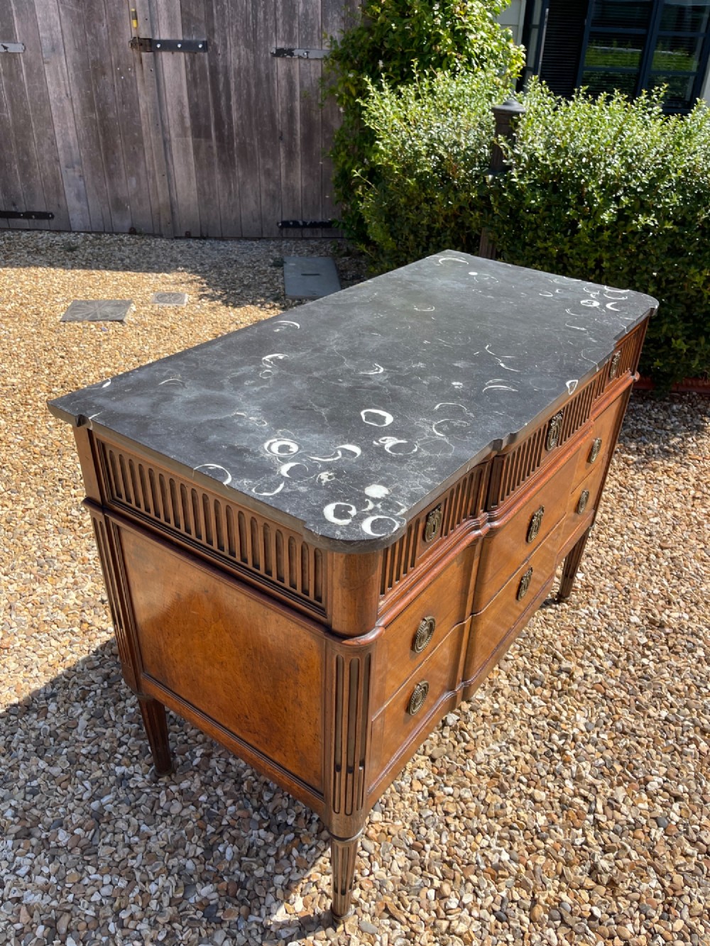 An 18th-century French cherrywood commode featuring a dark grey marble top, three frieze drawers above two long drawers, fluted sides, brass ring handles, and tapered legs. View VI