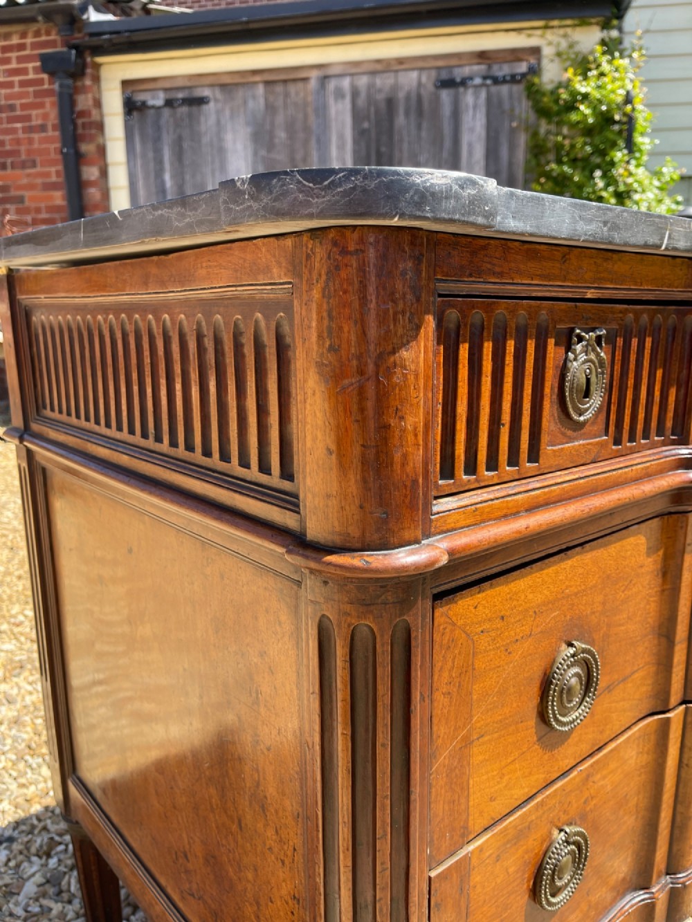 An 18th-century French cherrywood commode featuring a dark grey marble top, three frieze drawers above two long drawers, fluted sides, brass ring handles, and tapered legs. View VIII